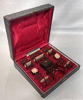 Original carrying case opened showing all miniature wooden furniture pieces fitted inside red satin-lined compartments.