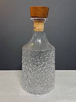 Front angled view of textured glass decanter with original teak stopper inserted showing the rough Glacier pattern texture on glass body and cork neck fitting
