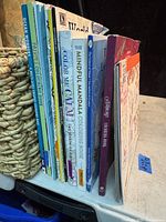 Side view showing spines of 13 adult coloring books, various titles and thicknesses.