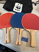 Three ping pong paddles displayed on a table, two StarCraft paddles with red and blue rubber, and one East Point paddle with red rubber.