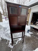 Closed view of the two-piece wooden cupboard with glass panel doors standing outside in winter conditions.