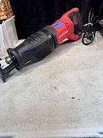 Side view of red and black Craftsman electric reciprocating saw with power cord visible, laid on a light-colored surface.