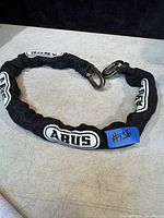 Full length view of ABUS heavy duty bike chain lock coiled displaying black sleeve with white ABUS logos.