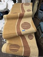 Photo showing the full length of the Art Deco style runner rug rolled out showing geometric circles and wavy lines pattern in beige, tan, and brown colors.