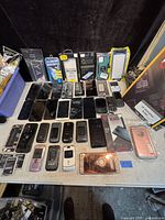 View of multiple smartphones, some with cracked screens, various brands and models, laid out on a table along with phone cases and screen protectors