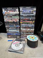 Wide view of two stacked columns of DVD movies showing titles and condition of cases along with loose DVDs in plastic bags.