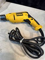Yellow and black DeWalt hammer drill drill driver with power cord coiled beside it on a white surface