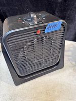 Front view of the black electric space heater and fan showing control dial and warning light