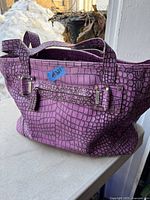 Side view of the purple croc-patterned bag with double straps and belt detailing