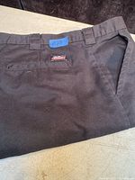Black men's work pants folded to show back pocket area and belt loops with a blue tape tag marked '#27'.