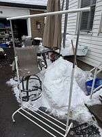 Front view of white metal clothes rack with adjustable height, standing outdoors in snowy setting.