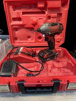 Milwaukee cordless impact drill, one battery attached, charger and extra battery inside the open red plastic case.