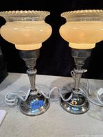 Pair of vintage boudoir lamps showing frosted glass shades with beaded edges and metal bases with on/off switches and white cords.