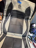 Photo showing the full front seat cover laid flat, displaying black and beige colors with embroidered logo and printed texts.
