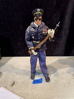 Full front view of the 11-inch vintage GI Joe Honor Guard figure dressed in dark blue uniform with medals, white gloves, black shoes, cap, sunglasses, and holding a rifle with bayonet.
