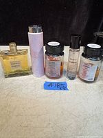 All five Chanel perfume bottles in a row on a beige surface against a black background.