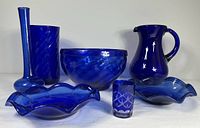 Seven blue glass items displayed together on white background showing variety of shapes and sizes