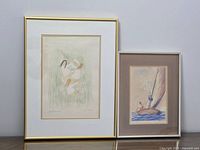 Photo showing two framed prints side by side against a wall, the 'Le pied des enfants' print in a gold frame on the left and the sailboat print in a silver frame on the right.