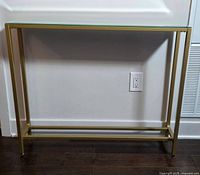 Front view of the console table against a wall, showing the gold-tone metallic frame and mirrored glass top.