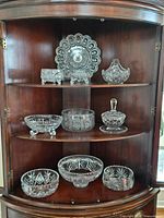 Full view of crystal and glass lot inside a wooden curio cabinet with multiple shelves showing all items