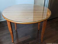 Round wooden dining table with clear removable round glass top, wood grain visible, four curved wooden legs, photographed from an angle showing full glass surface.