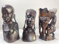 Front view of three different-sized African wood hand-carved busts and figures arranged side by side.