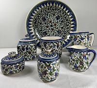 Photo showing entire set of Jerusalem pottery including a large bowl, large pitcher, small round canister with lid, and other pottery pieces with intricate floral designs.