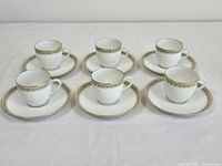 Set of six demitasse cups and matching saucers arranged on a white surface, showing consistent pattern and style.