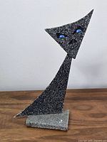 Front view of the signed metal cat sculpture showing the blue eyes and textured surface.