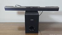 Black Philips soundbar positioned on top of the black rectangular subwoofer with Philips logo and front bass port.