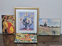Four framed and unframed art pieces arranged on table, includes floral and music themed prints and paintings.