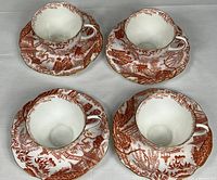 Top-down view of four teacups on their matching saucers, showing the red oriental pattern with figures, pagodas, and nature scenes.