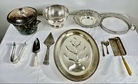 Full lot of silver plated serving pieces including trays, ice bucket, servers, spoons, and tongs arranged on white cloth