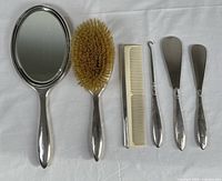 Full set laid out on white fabric: hand mirror, hairbrush, comb, large shoehorn, two small shoehorns