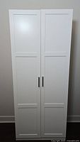 Full front view of white storage cabinet with two panel doors and metal handles