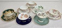 Overview image showing 7 assorted teacups and matching saucers with various vintage floral and classical designs.