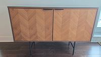 Front view of Structube Tignor TV cabinet / sideboard with chevron wood veneer pattern on doors and black metal legs.