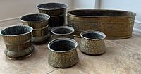 All eight brass planters displayed together on tile floor.