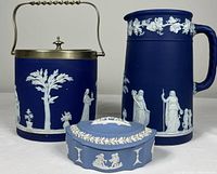 Photo showing the biscuit barrel, water jug, and covered trinket box together, highlighting the blue jasperware with white relief decoration and metal lid on barrel.