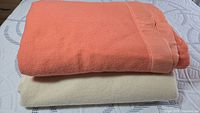 Both folded blankets shown stacked; peach wool mixed blanket on top, cream Esmond wool blanket underneath