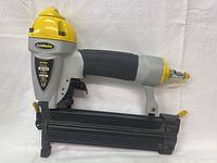 Side view of the TradeMaster pneumatic air nailer/stapler showing ergonomic grip, nail/staple magazine, trigger, and air hose connector.