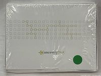 Front of sealed AncestryDNA kit box showing the logo and gold square design on white background.