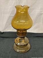 Full view of the antique amber glass oil lamp showing amber glass chimney with scalloped rim and clear glass base on a black cloth background.