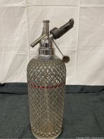 Front view of antique Sparklets seltzer siphon with wire mesh casing and metal siphon top