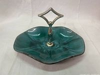 Angled view of the bluish-green ripple drip glazed pottery tidbit dish with a silver-tone removable handle showing the dish's shape and glaze texture.