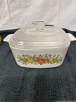 White Corning Ware casserole dish with vegetable pattern and clear glass lid, shown from front angle.