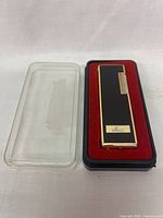 Dunhill Rollagas lighter in protective case showing black lacquer front with 'Mai' inscription and gold-tone sides.