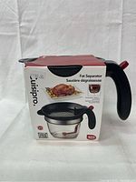 Photo of Luispro Fat Separator in box showing front with product name and image of fat separator tool holding a serving of turkey.