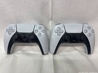 Front view of two PS5 DualSense controllers side by side on white cloth background.