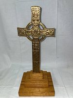 Front view showing detailed embossed brass cross with ring design on wooden stand.